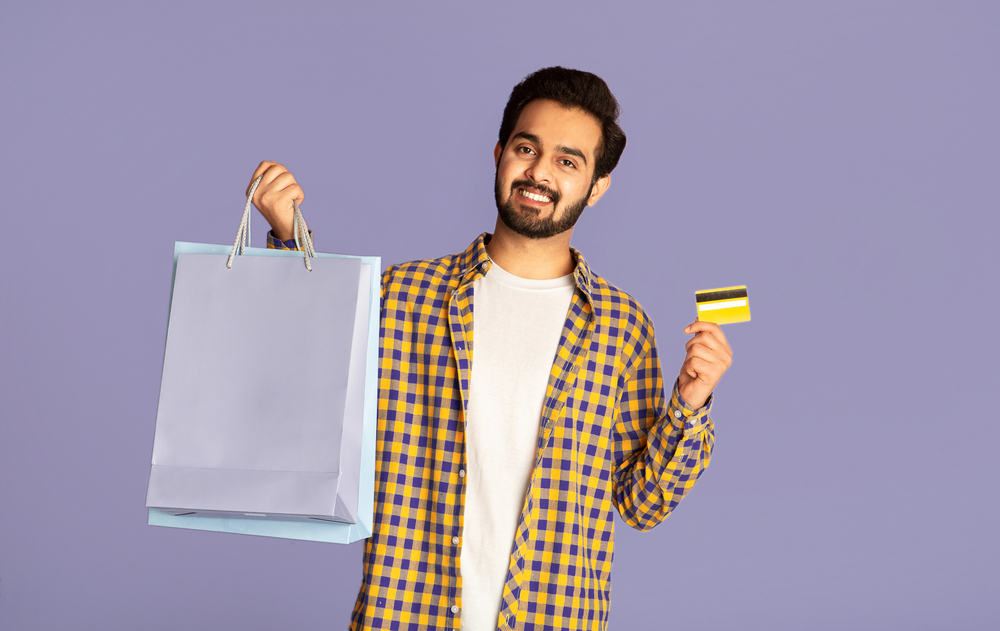 consumer in india - Smiling Indian man holding shopping bags and credit card on violet background - borzo